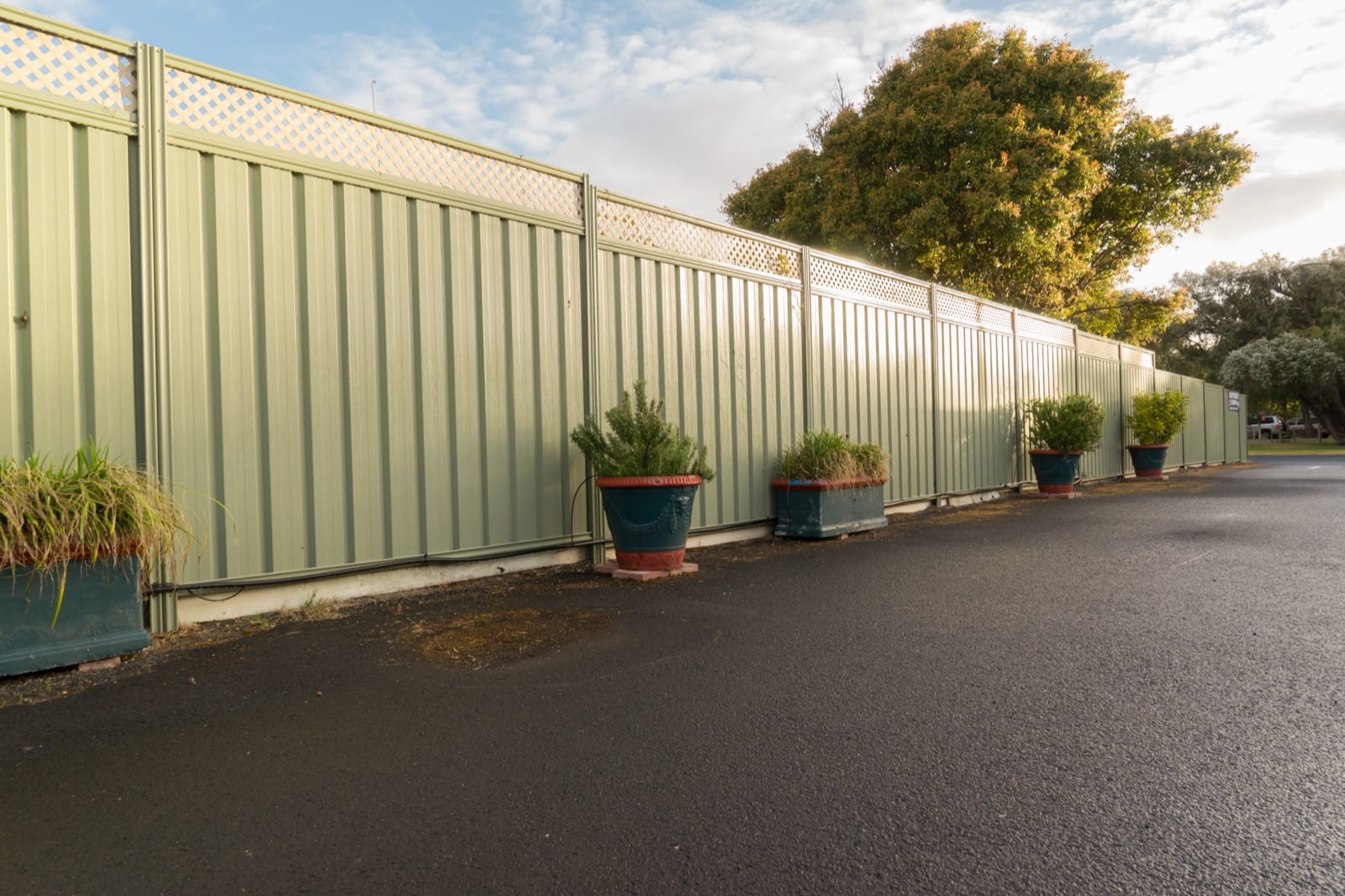 Colorbond privacy fence with lattice top and potted plants along a paved driveway in an Apex, NC HOA community