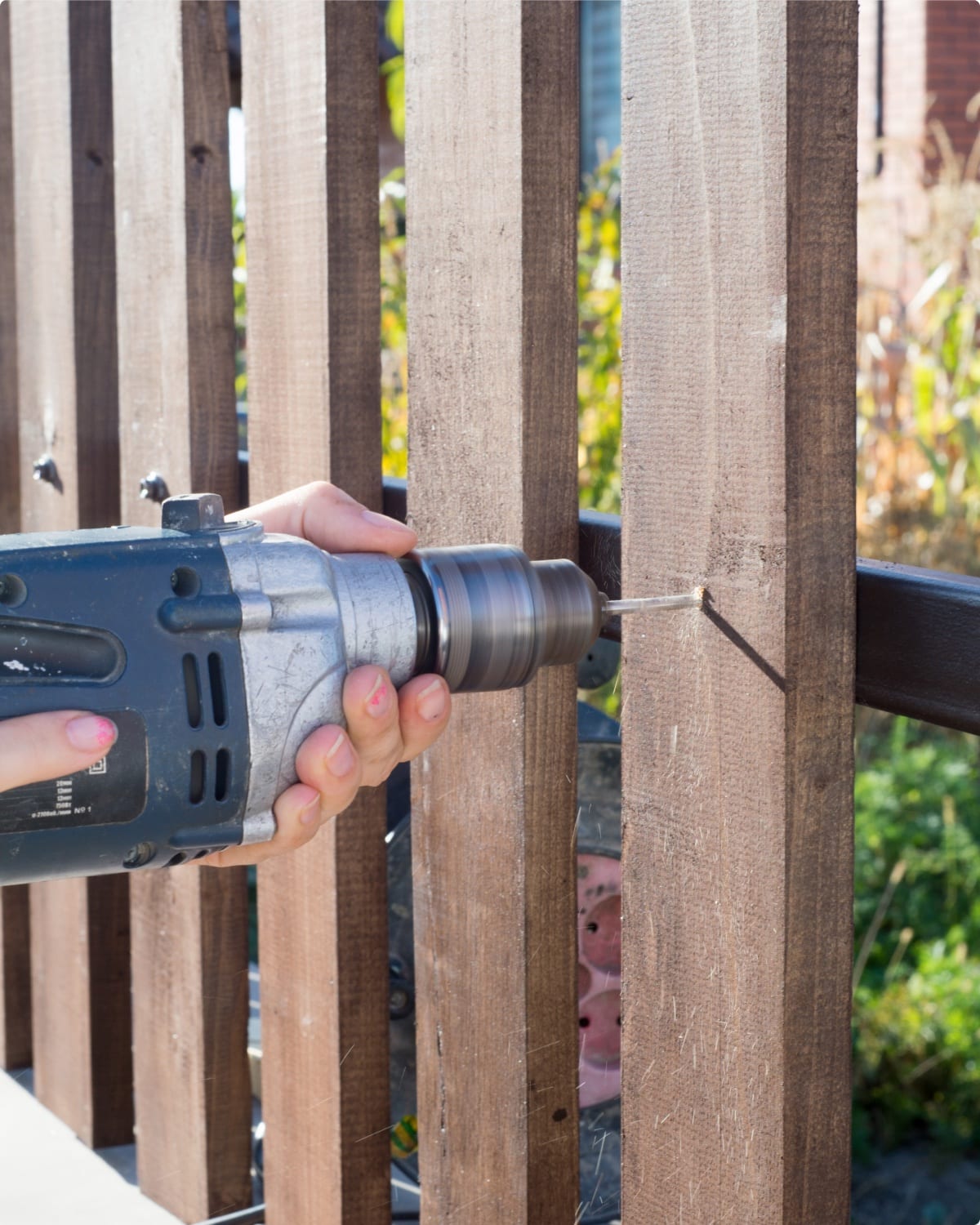 Fence Works installer drilling into a wooden fence rail in an Apex, NC backyard