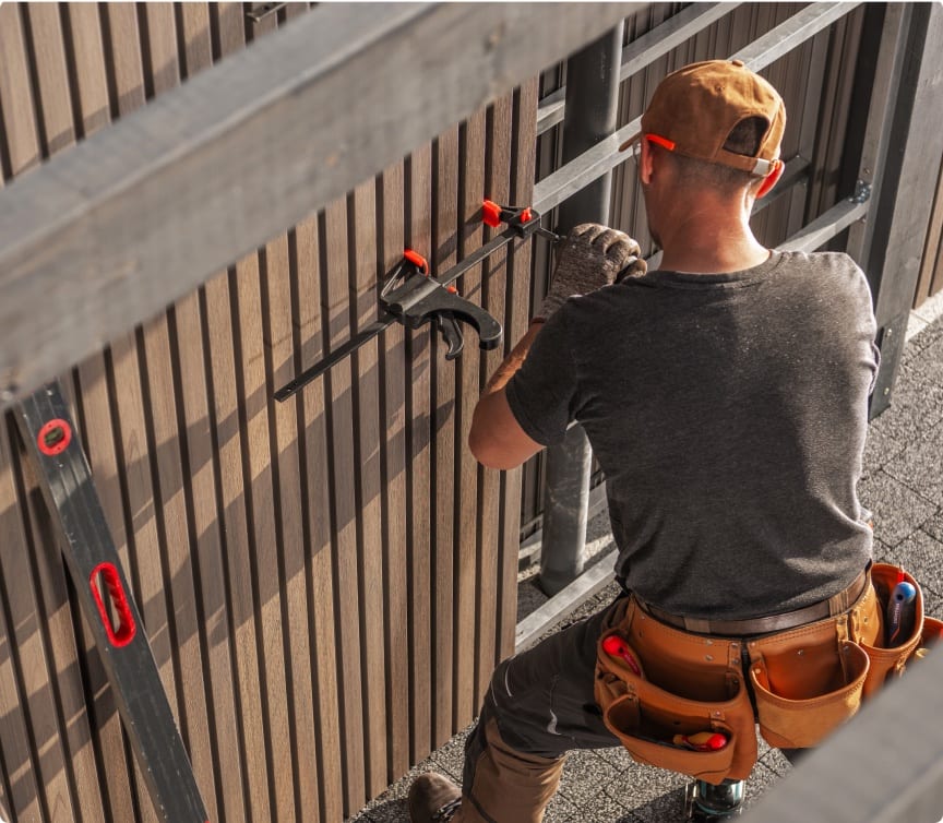 Installer with a tool belt fastening boards on a fence at a tidy job site
