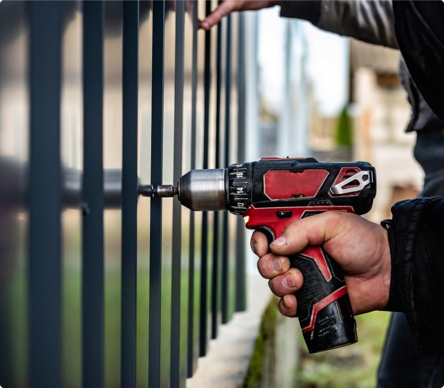 Close-up of a power drill fastening a panel on an aluminum fence