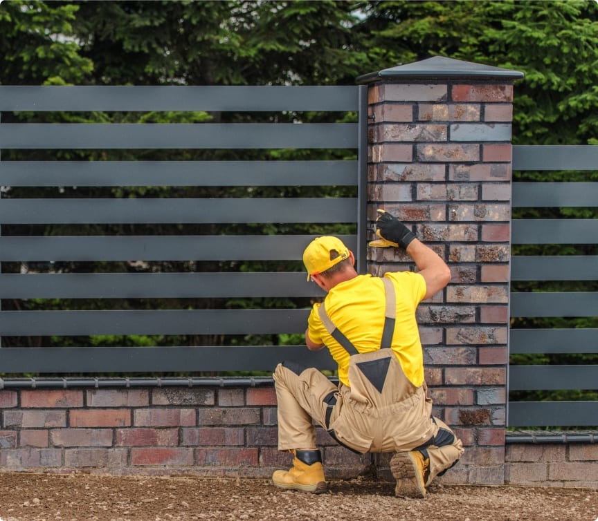 Experienced fence installer in safety gear building a fence beside a brick column